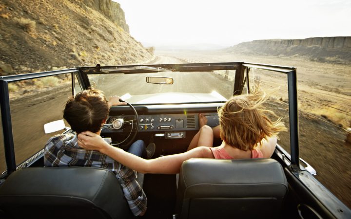 Young couple driving convertible at sunset