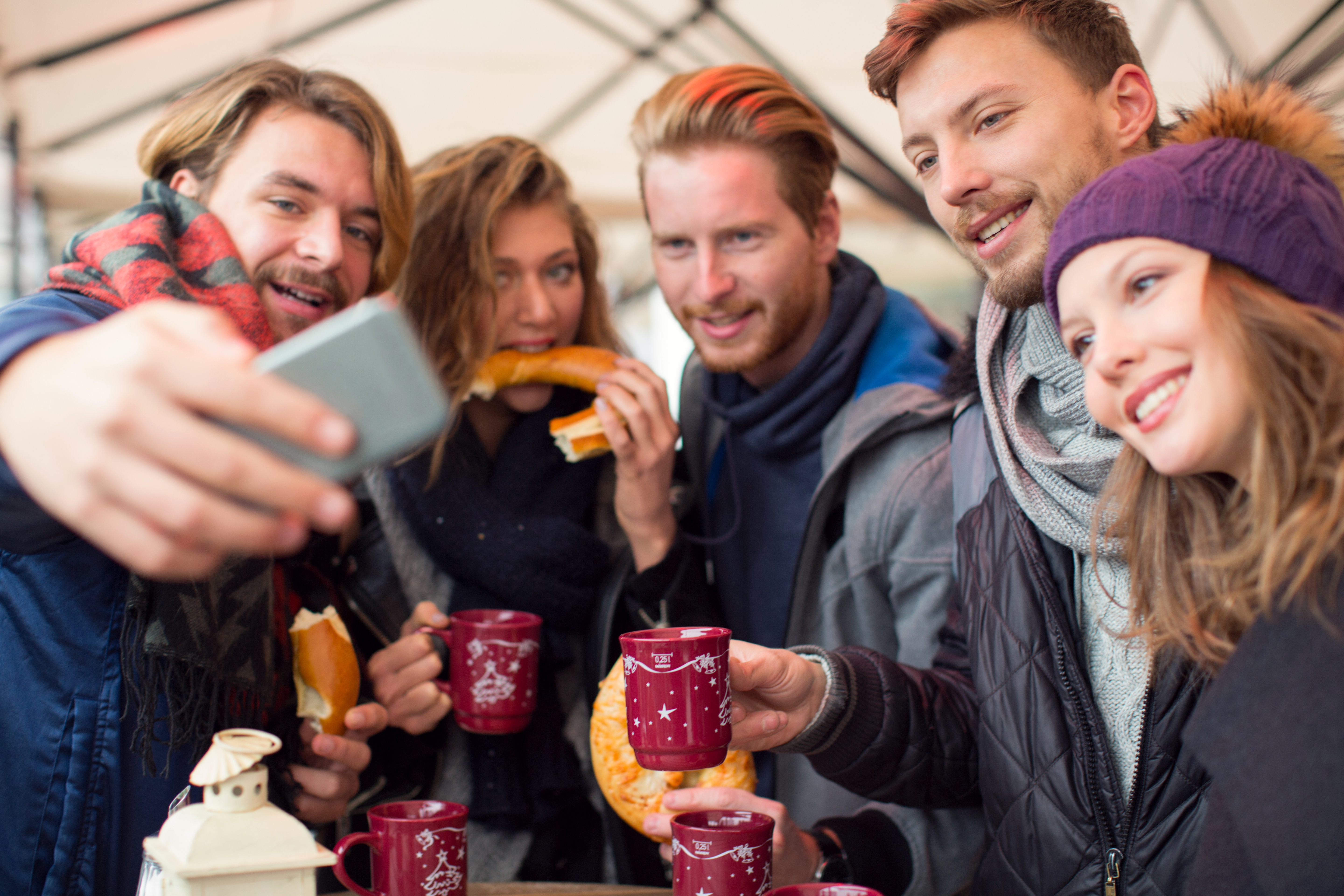 Friends drinking hot wine and eating pretzels at outdoor cafe on a street, christmas market. Wearing warm clothes, holding mugs and taking selfies with smart phone. Vienna, Austria.
