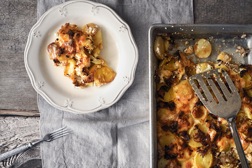 Tartiflette in the baking tray with slice on the plate top view